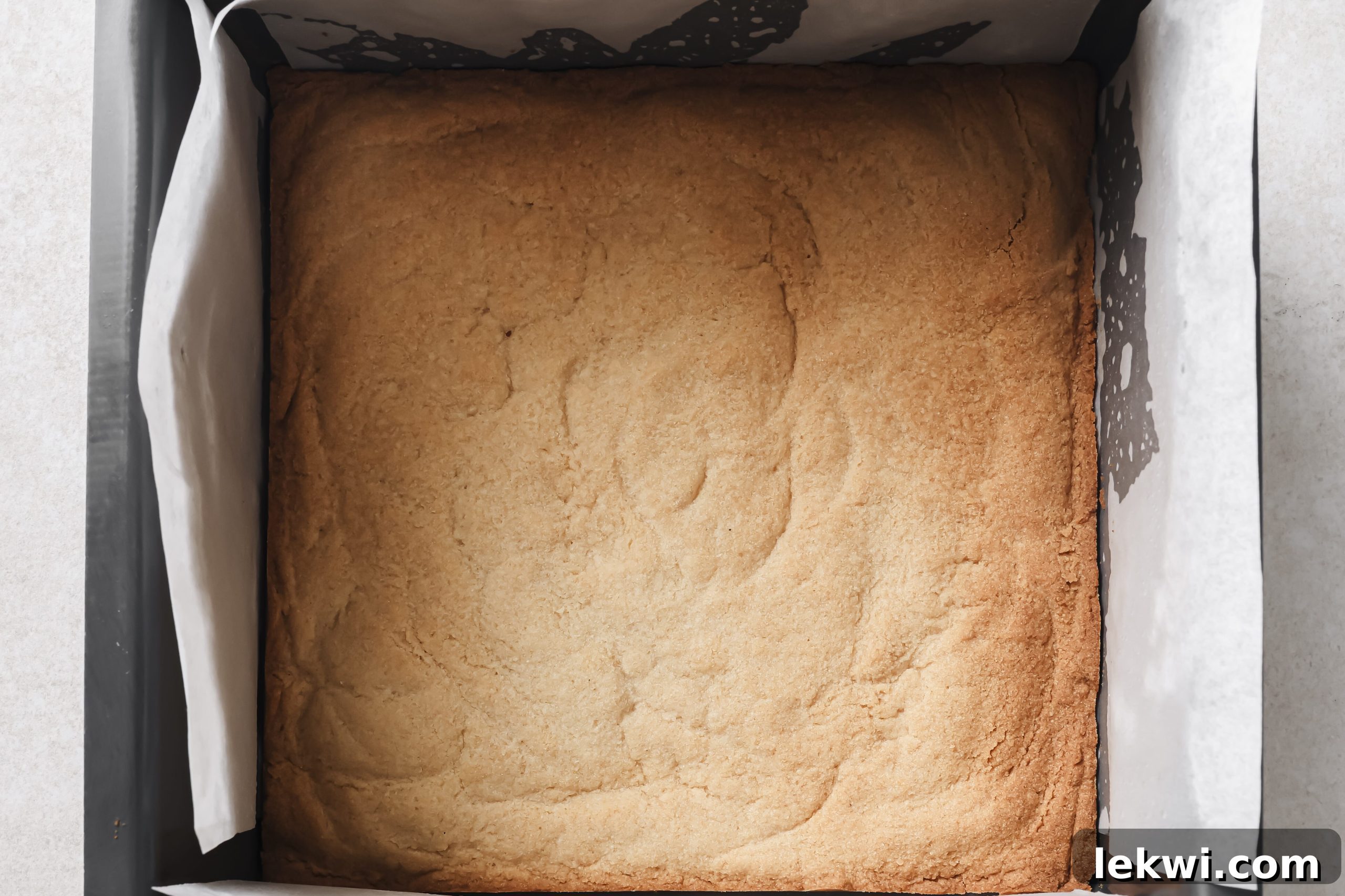 The baked pumpkin pie bar crust sitting in a baking pan lined with parchment paper, golden brown and cooled.