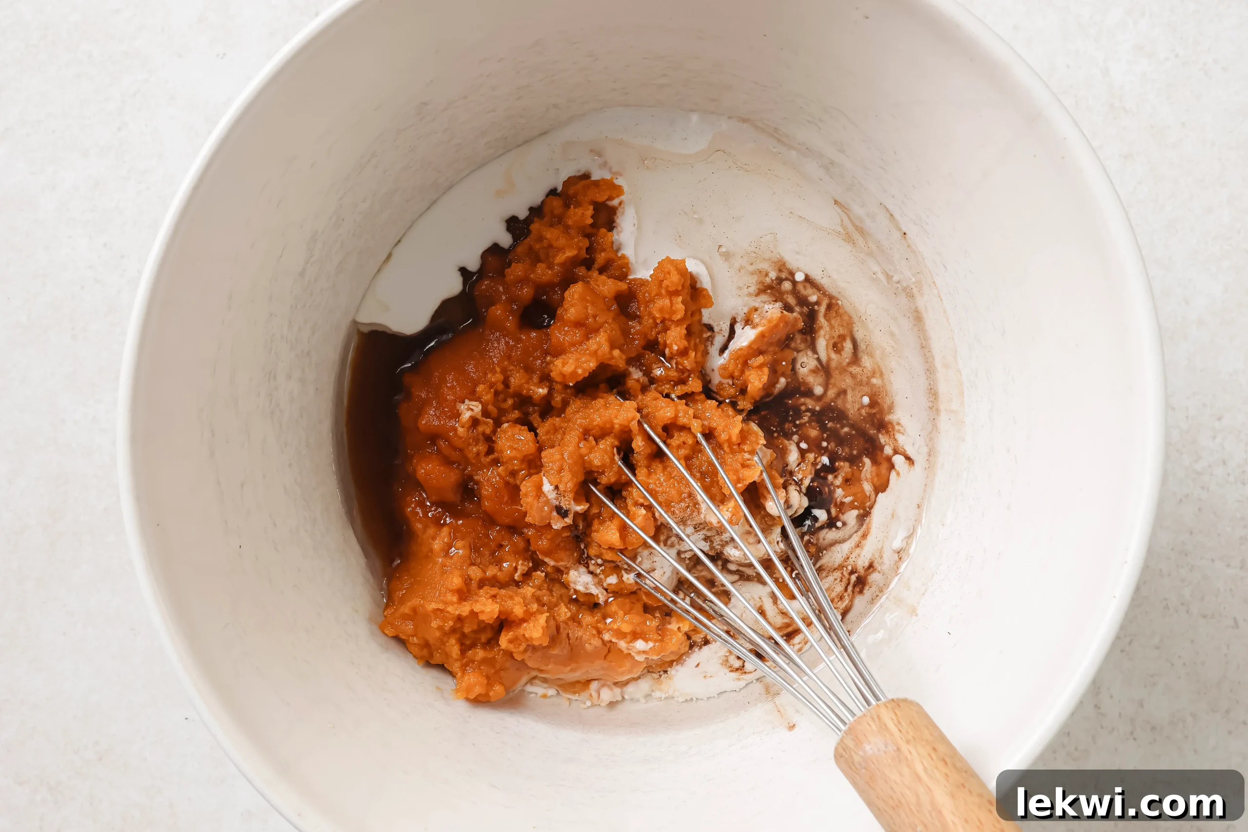 All the ingredients for the pumpkin pie bar filling, including pumpkin puree, coconut cream, and spices, unwhisked in a large bowl.