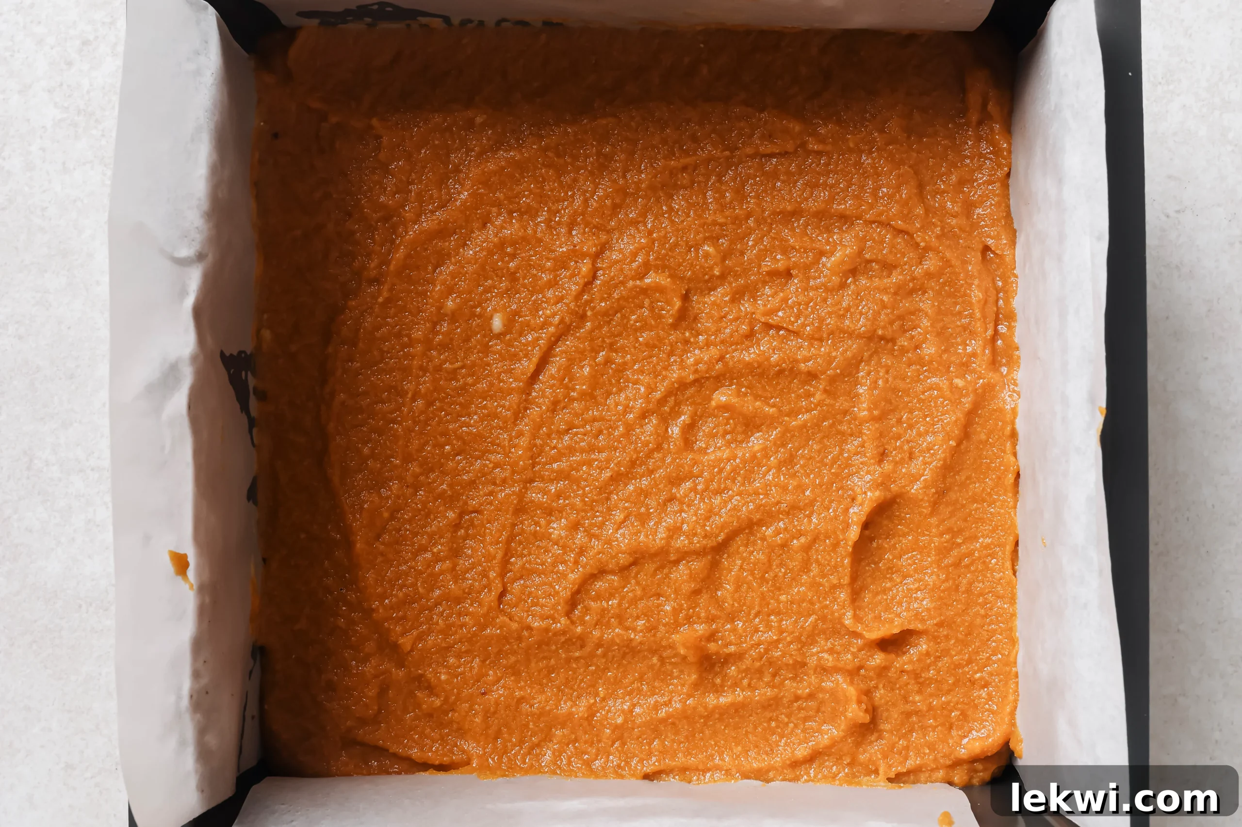 The smooth pumpkin pie bar filling carefully poured over the cooled, baked crust in the baking pan, ready to be chilled.