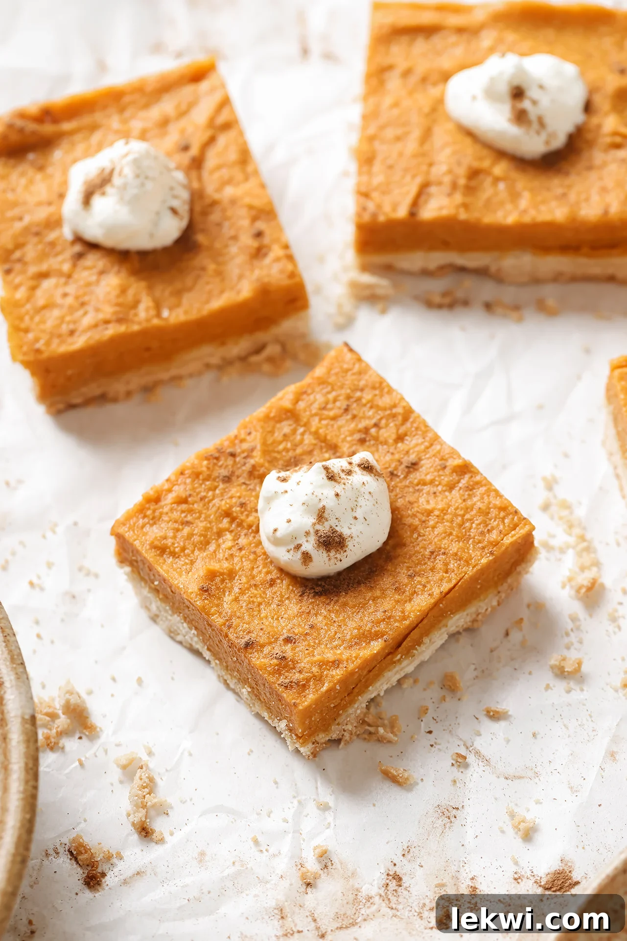 Three AIP pumpkin pie bars arranged on parchment paper, beautifully garnished with coconut cream and a dusting of cinnamon.
