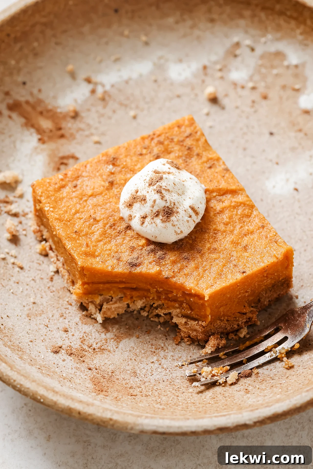 One pumpkin pie bar on a plate topped with coconut cream and cinnamon.