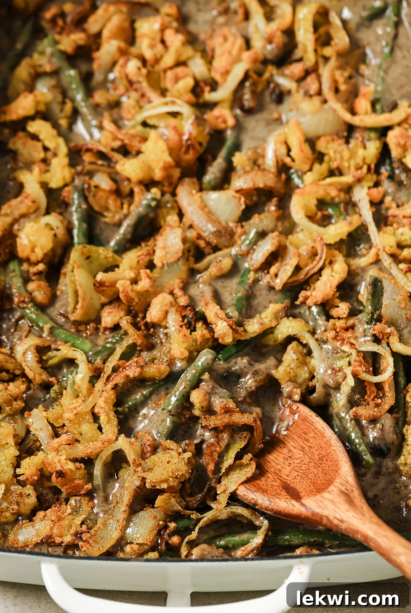 Green bean casserole in a large baking dish with a wooden spoon, showcasing its golden-brown topping and creamy texture.