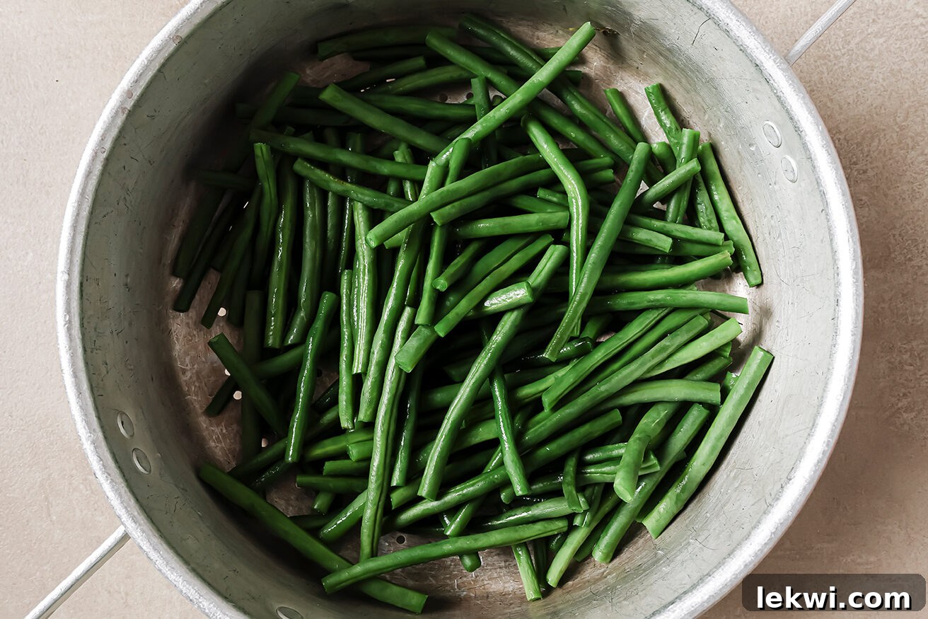 Blanched green beans coated in cream of mushroom soup in a large mixing bowl.