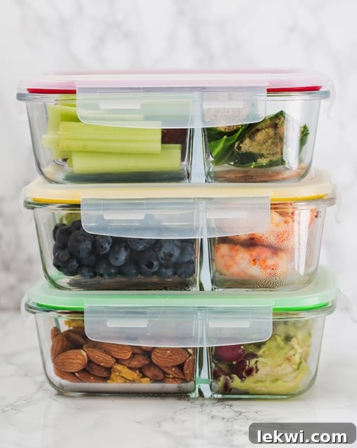 Three glass tupperwares, neatly stacked, filled with colorful cut fruit and vegetables for meal prepping.