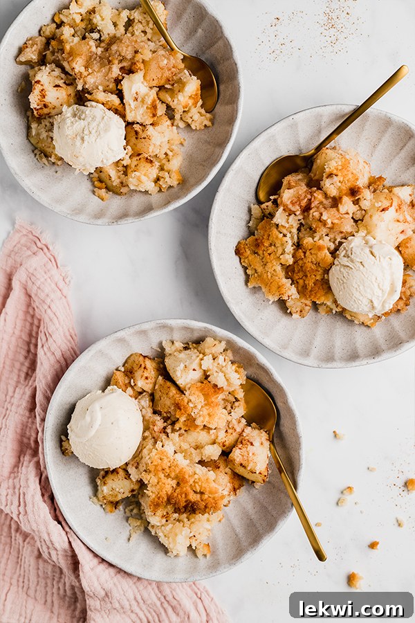Warm apple crisp served in individual plates, accompanied by spoons and scoops of vanilla ice cream.