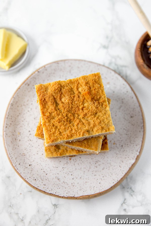 A stack of golden grain-free cornbread squares rests on a grey plate, accompanied by a small dish of butter.