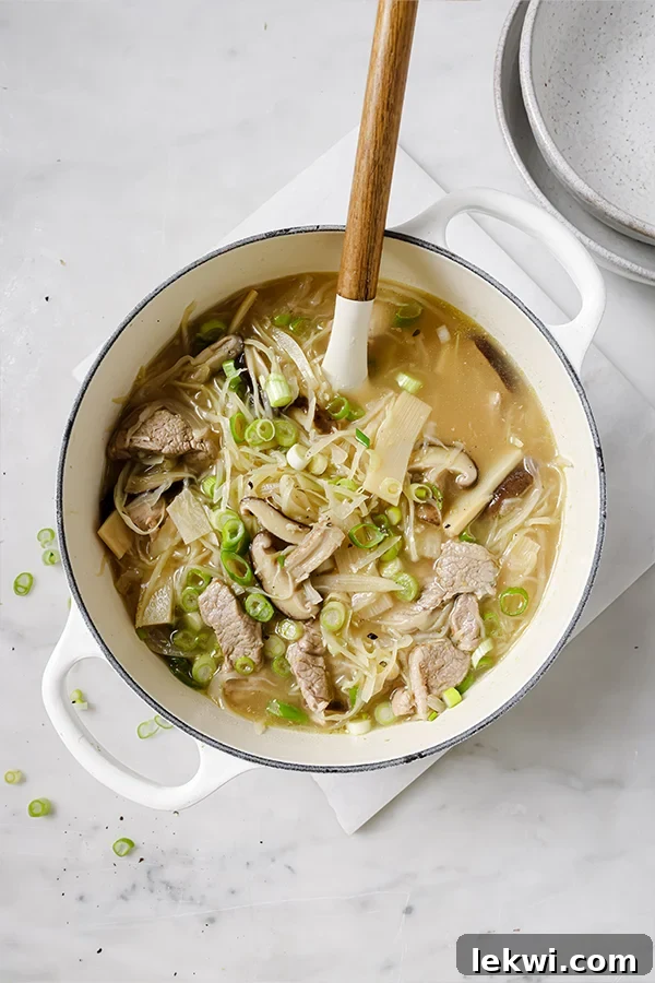 A Dutch oven filled with steaming hot and sour soup, garnished with fresh green onions.