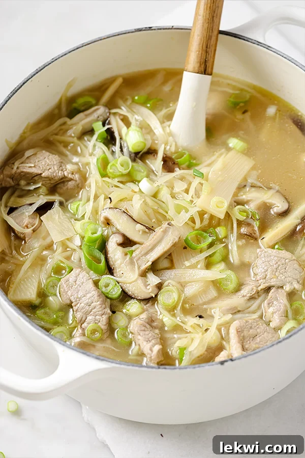 A large pot of hot & sour soup, with a serving spoon stirring the rich, flavorful broth and ingredients.