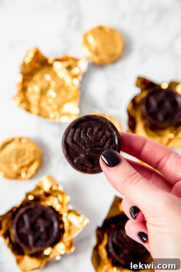 A hand holds a perfectly wrapped Hanukkah gelt coin, glistening in gold foil.