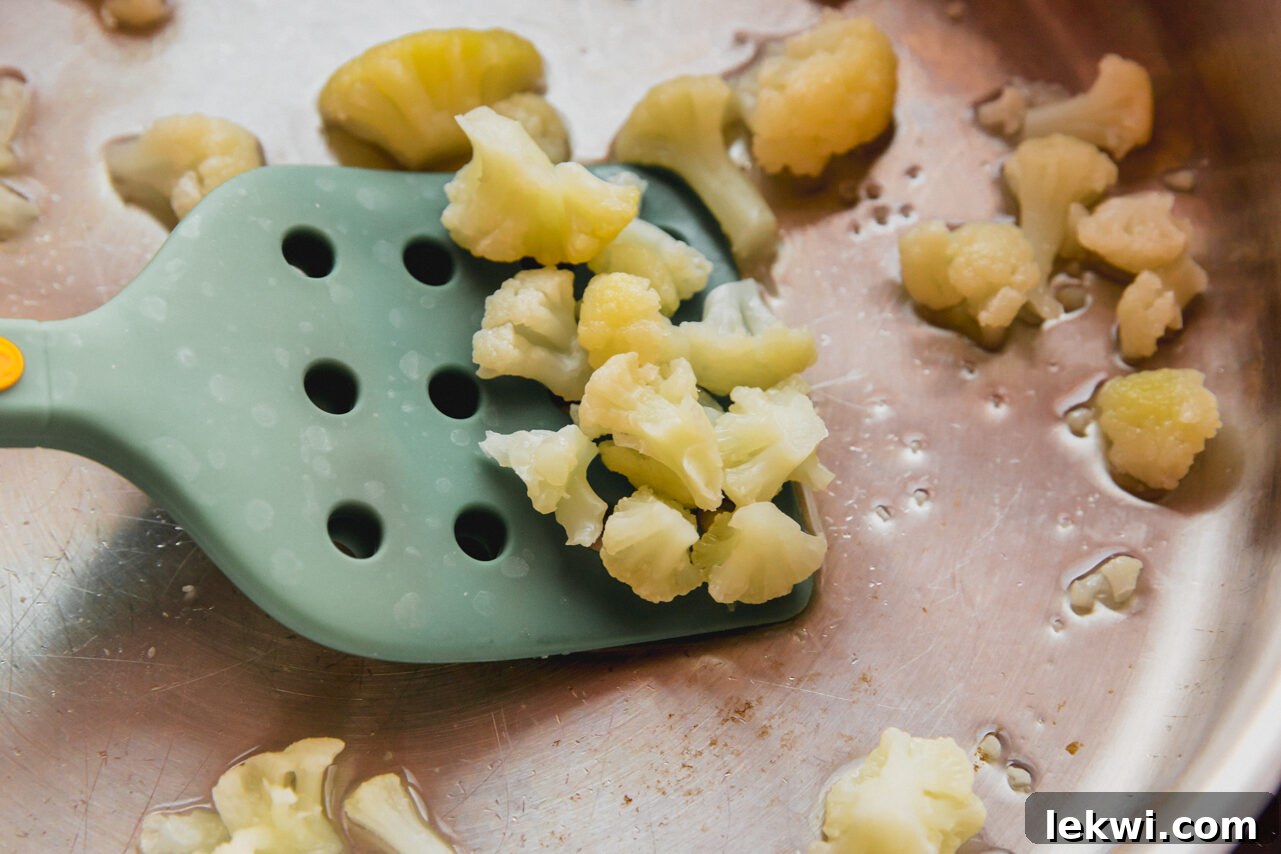 Cauliflower florets being scooped by a spatula from a pan after steaming until tender.