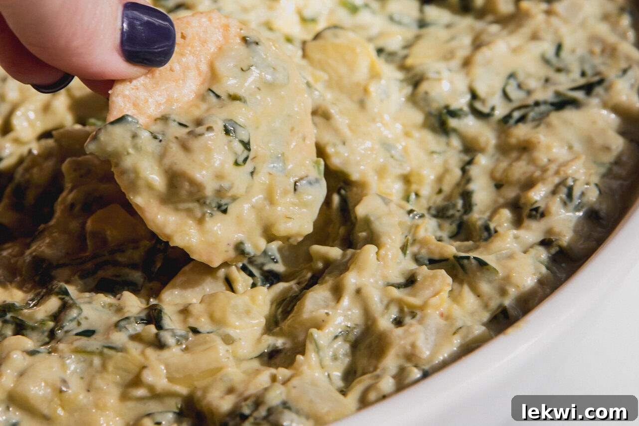 A cracker scooping up a generous portion of the finished dairy-free spinach and artichoke dip, ready to be enjoyed.