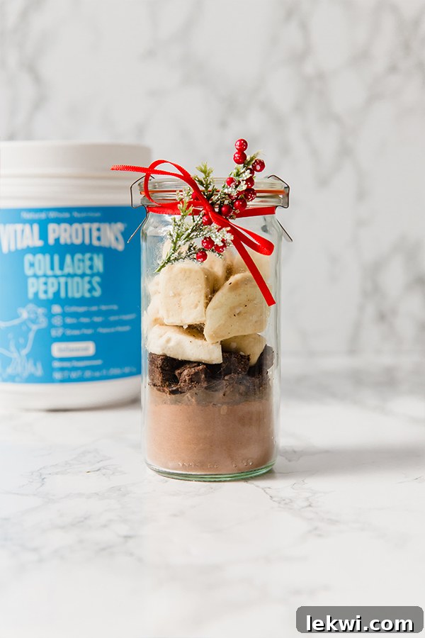 A single glass jar elegantly filled with the DIY collagen hot cocoa mix and topped with marshmallows, tied with a festive red ribbon.