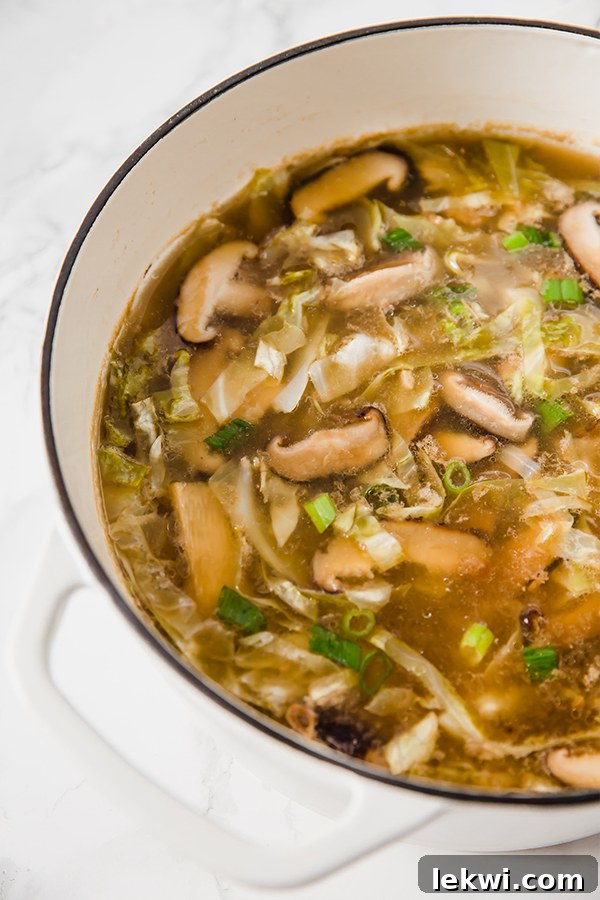 A pristine white Dutch oven, gently bubbling with a fresh batch of flavorful hot and sour soup, invitingly ready for serving.