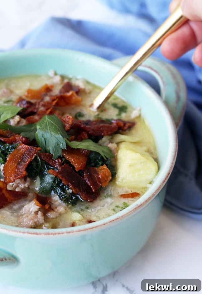 A vibrant blue bowl filled with rich, creamy Paleo Zuppa Toscana soup, generously topped with crispy bacon bits and fresh herbs, ready to be savored.
