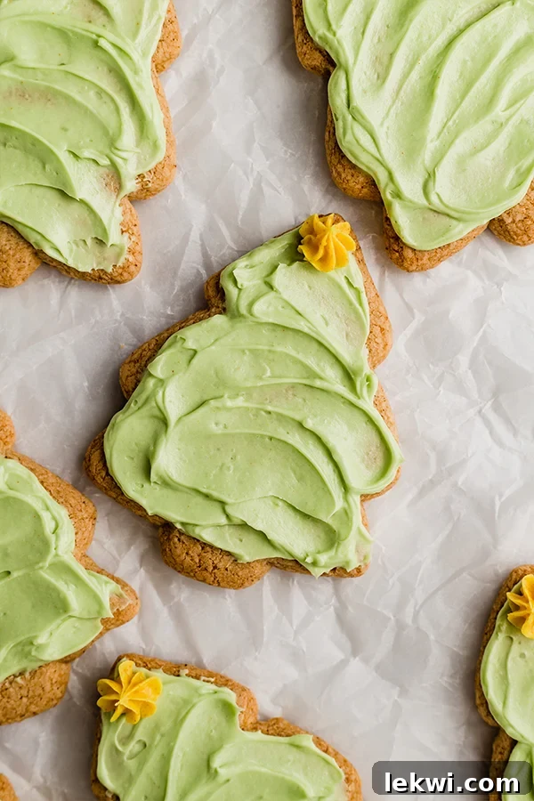 A sugar cookie shaped like a Christmas tree with green icing and a yellow icing star on top surrounded by other sugar cookies.