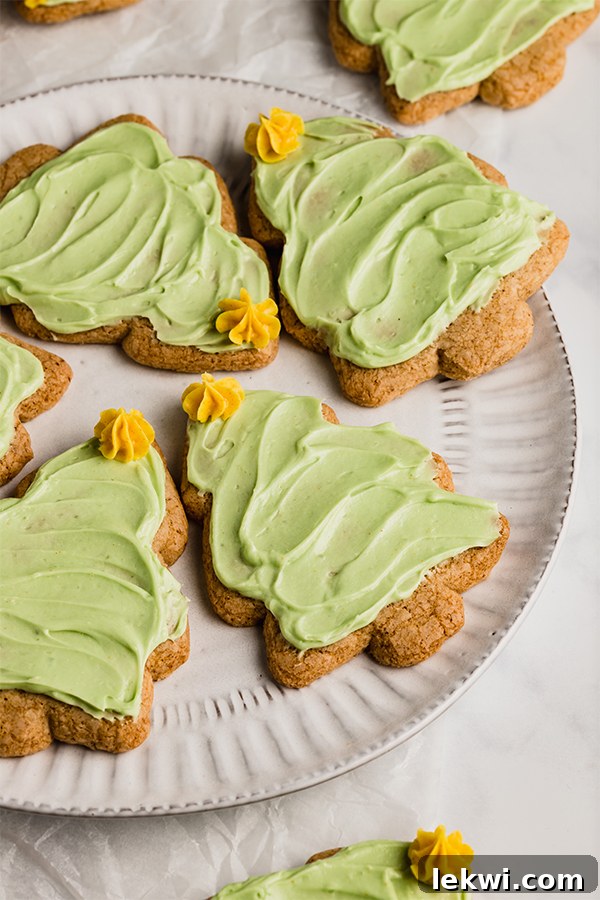 A white plate topped with sugar cookies cut out like Christmas trees and topped with green icing and yellow icing stars.