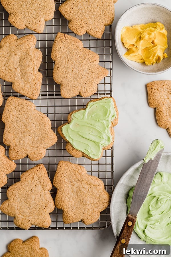 A wire rack topped with christmas tree sugar cookies with one iced with green icing. 