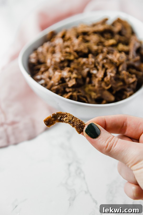 A white bowl filled with paleo coconut puppy chow with a hand holding one piece of puppy chow out in front.