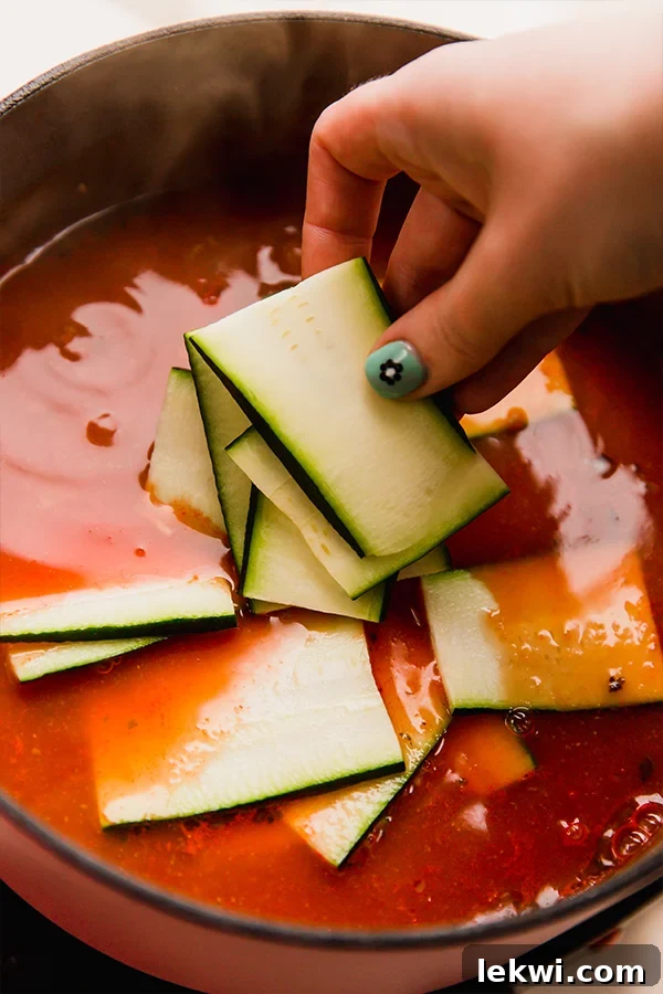 Person adding zucchini slices to a soup.