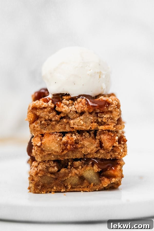 A stack of three apple pie bars topped with a scoop of vanilla ice cream.