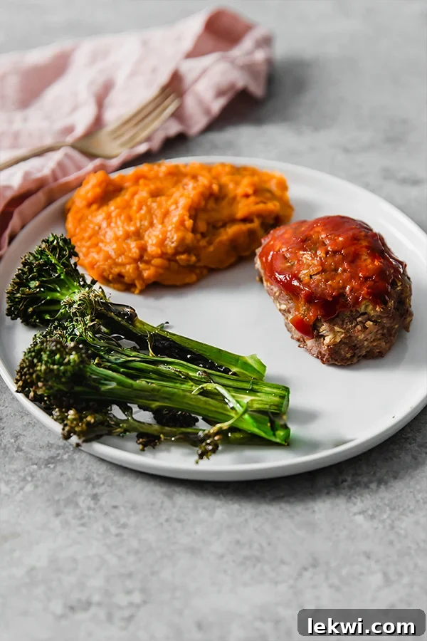 A white plate featuring a slice of homemade meatloaf, creamy mashed sweet potato, and perfectly roasted broccolini.