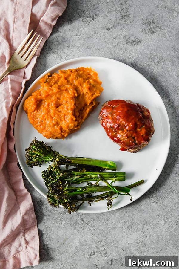A perfectly plated dinner showing mashed sweet potato, roasted broccolini, and a juicy slice of meatloaf.