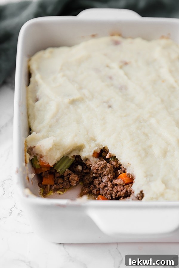 A large casserole dish filled with baked Low-Carb Shepherd's Pie, with one serving elegantly scooped out, revealing the savory meat filling and golden cauliflower topping.