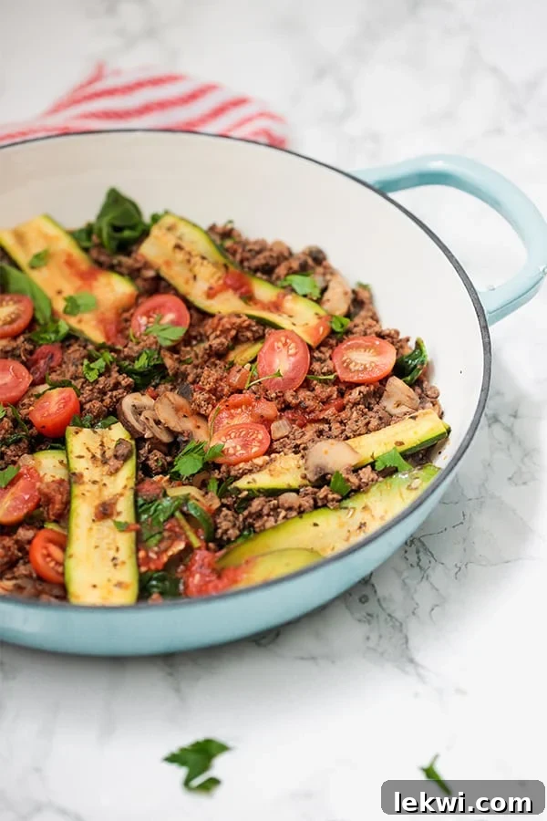 A vivid blue skillet overflowing with a hearty one-pot lasagna, featuring tender zucchini, rich tomato sauce, savory ground beef, and fresh herbs.