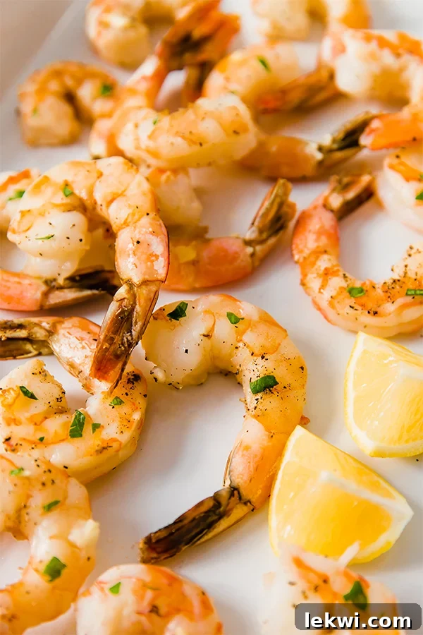 Brightly lit lemon baked shrimp on a baking sheet, garnished with fresh parsley and lemon wedges.