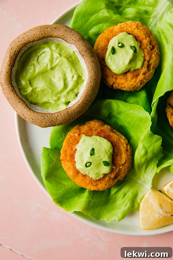 Close-up of baked Sweet Potato Crab Cakes topped with creamy Avocado Horseradish Mayo and fresh green onions.