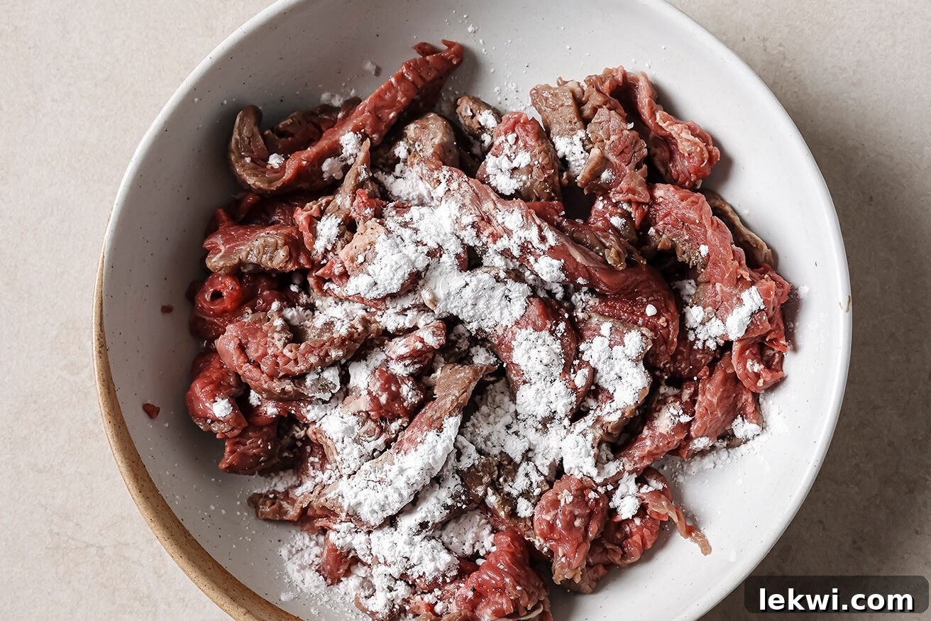 Thinly sliced flank steak being coated with arrowroot starch in a bowl.