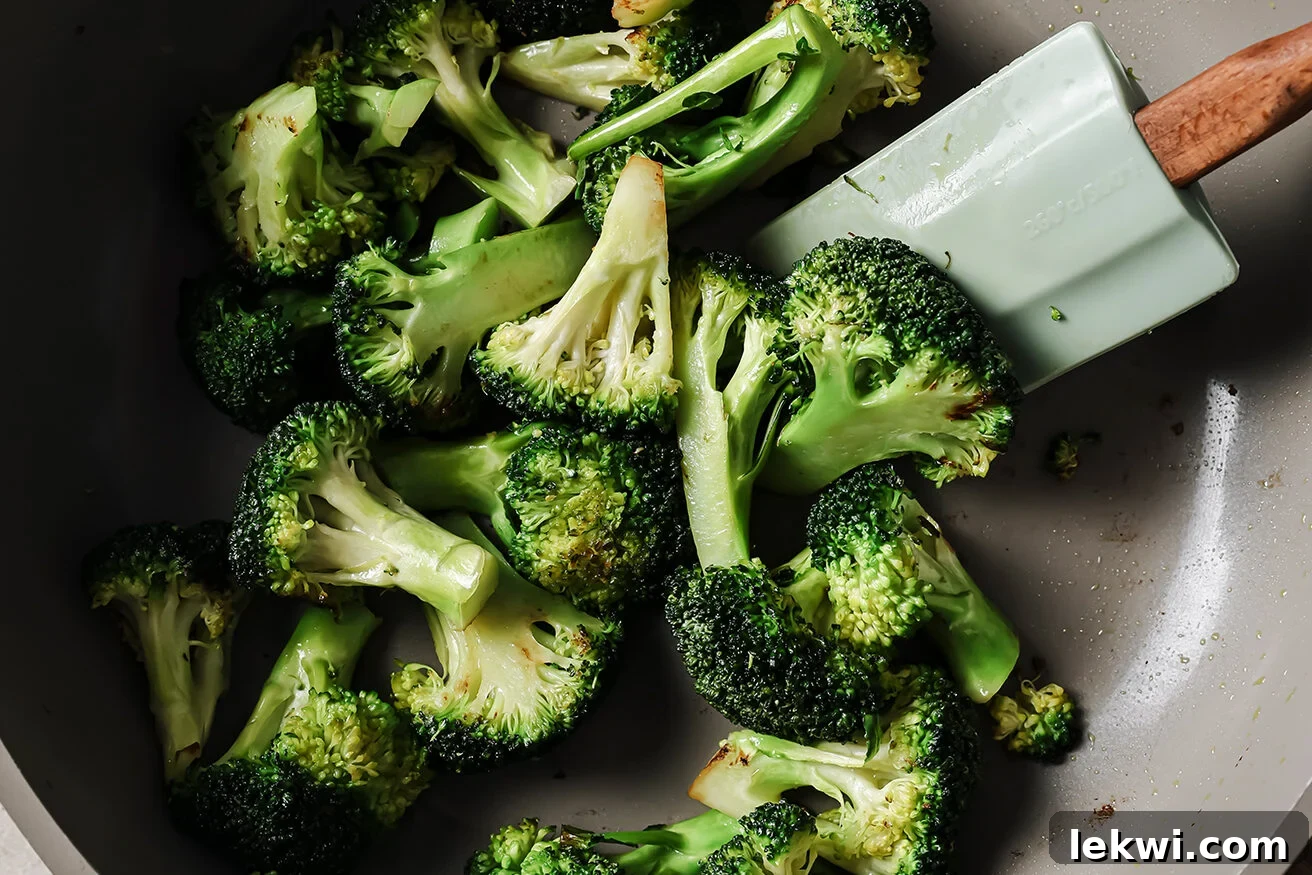 Broccoli florets being stir-fried in a pan with a spatula.