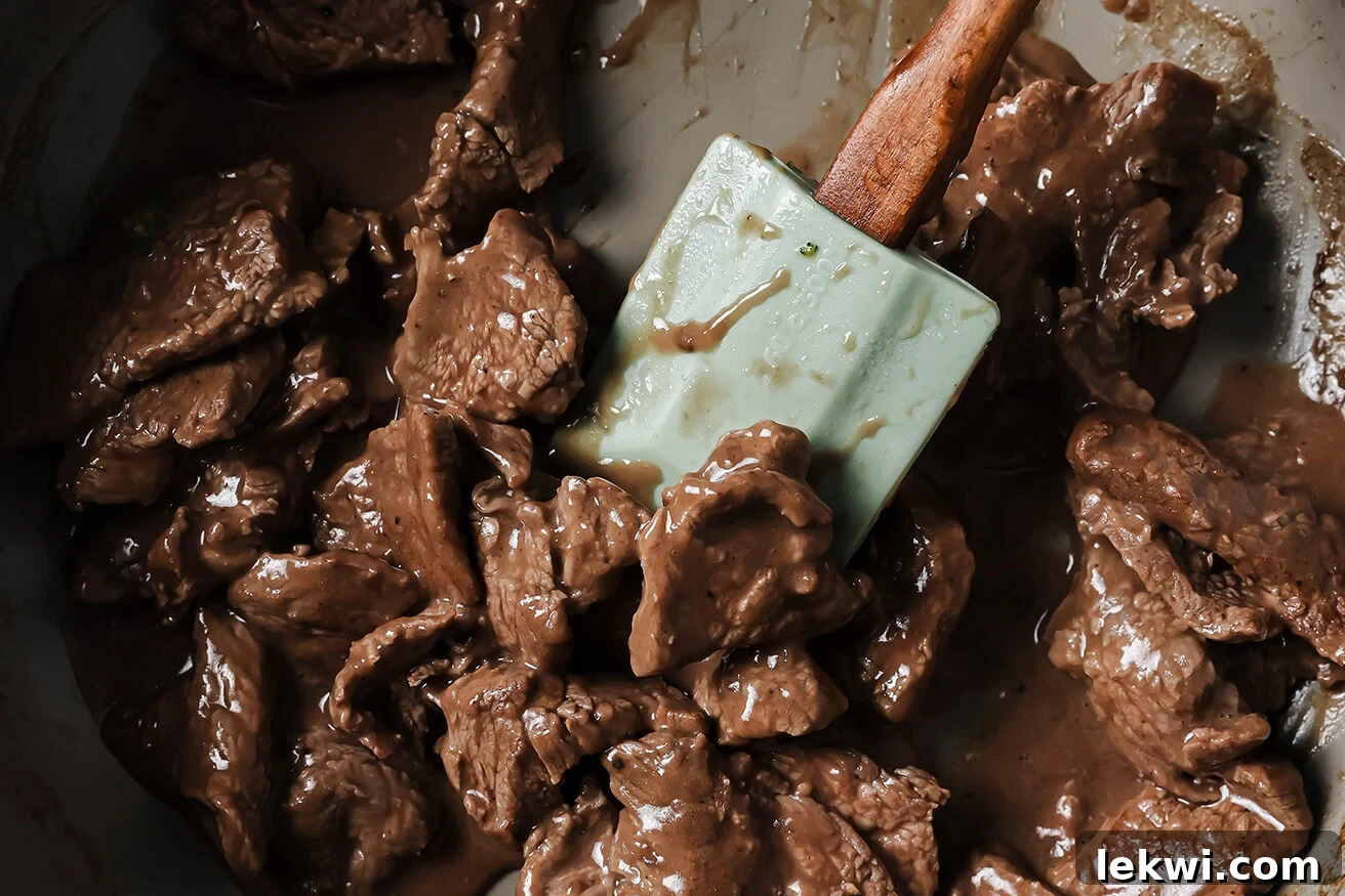 Cooked Mongolian beef being tossed in the simmering sauce in a pan.
