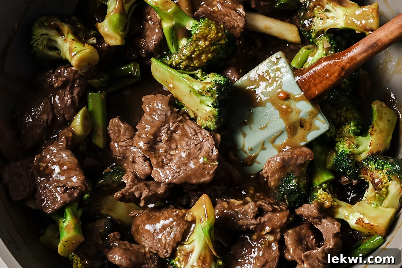 Mongolian beef and broccoli coated in sauce, simmering in a pan.