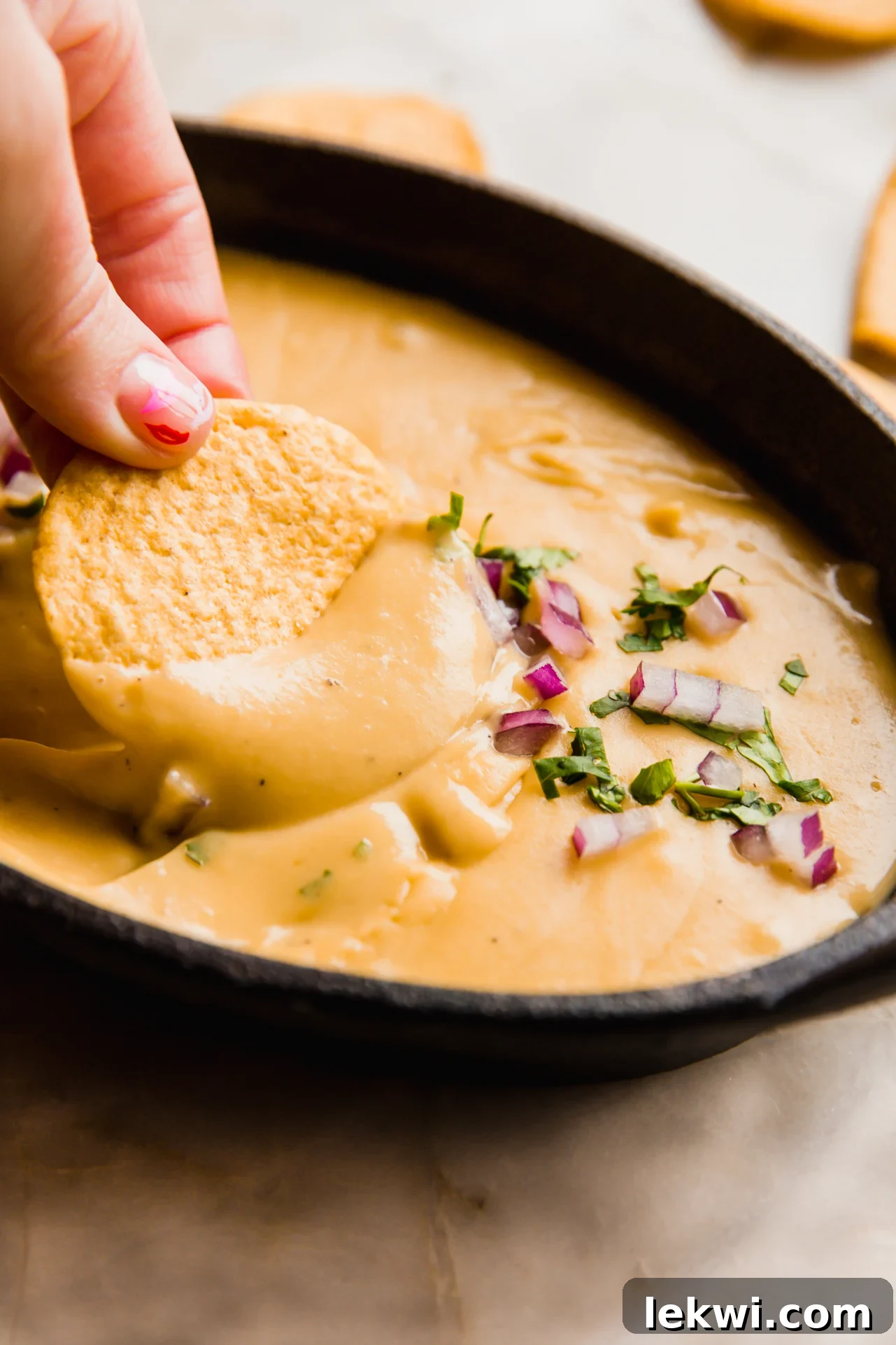 Grain free chip dipping into dairy free queso, showcasing its creamy texture.