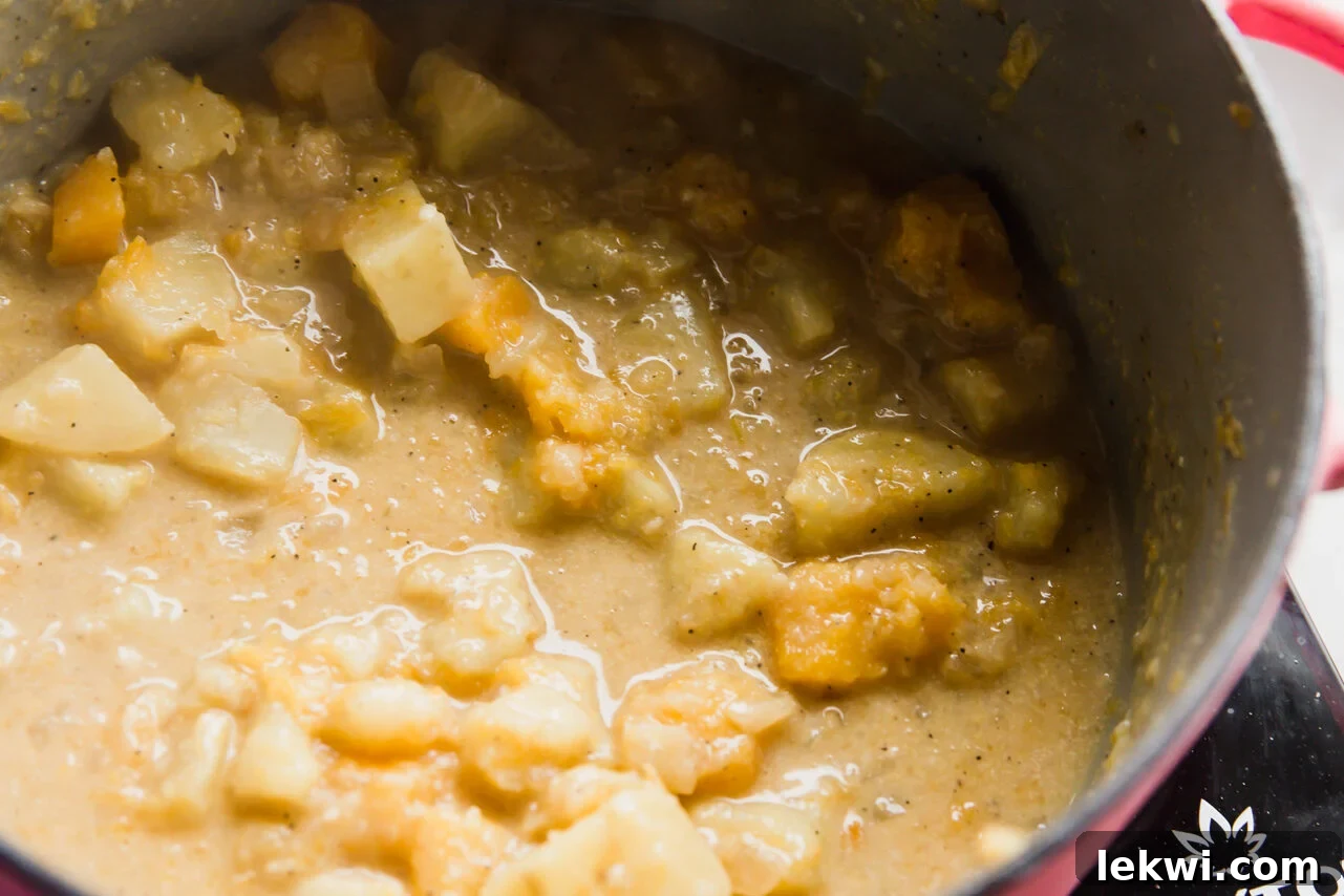 Thickened vegan queso in a pot, unblended, showing tender vegetables.