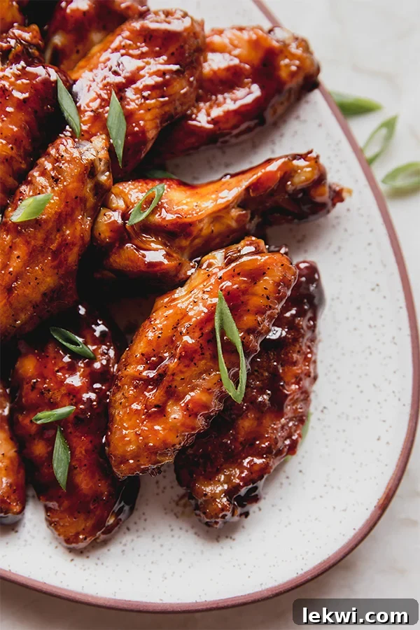A vibrant plate of General Tso-style Asian chicken wings, sticky and glistening with sauce, garnished with fresh green onions.