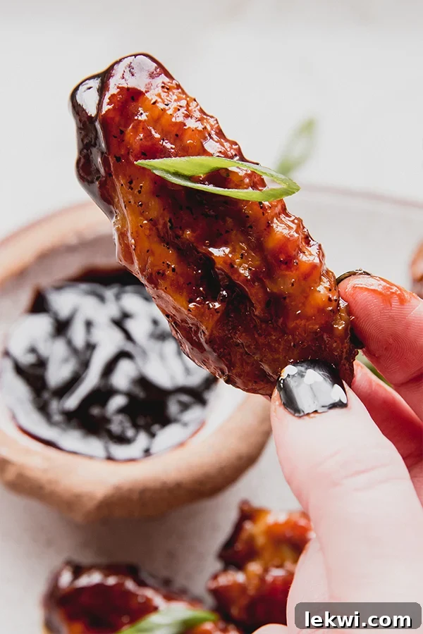 A hand holding a perfectly coated General Tso's style chicken wing, ready to be enjoyed.