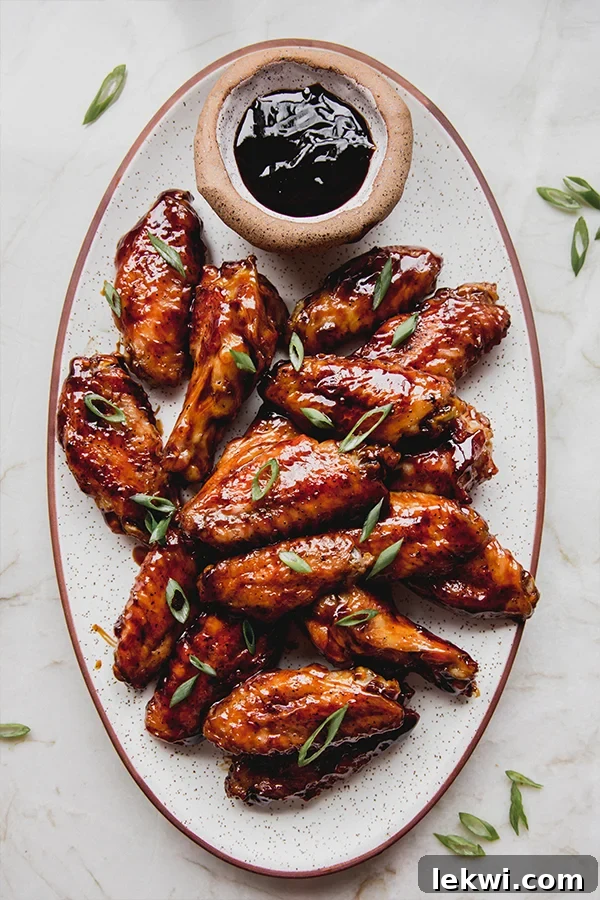 A large platter generously filled with sticky, glistening General Tso's style chicken wings, garnished with chopped green onions, ready to be shared.