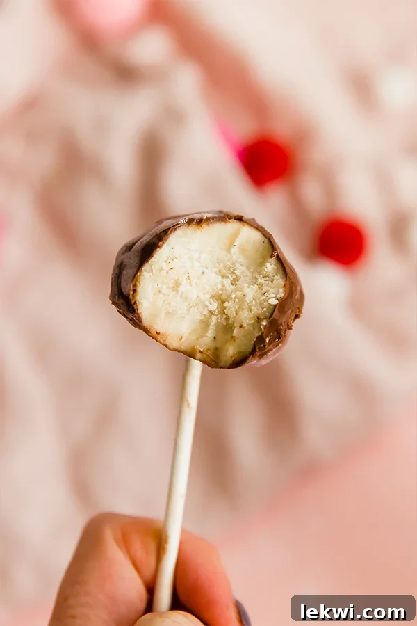 A cake pop with a bite taken out of it being held up against a fuzzy pink background.