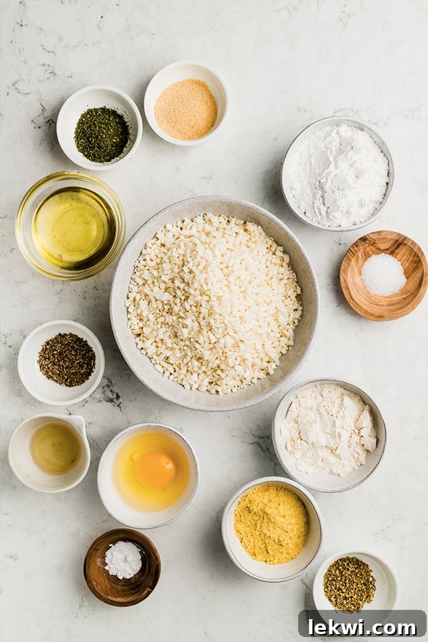A top-down view of the individual ingredients laid out on a clean surface, including riced cauliflower, arrowroot starch, coconut flour, nutritional yeast, olive oil, egg, and a selection of dried herbs and spices, all neatly arranged for making cauliflower breadsticks.
