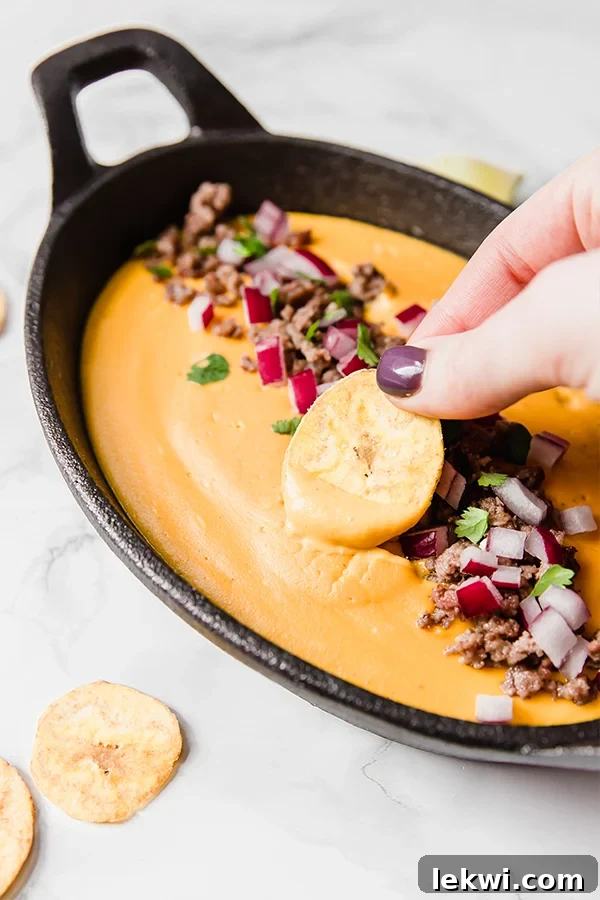 Person dipping a chip into creamy dairy-free queso, perfect for game day snacking.
