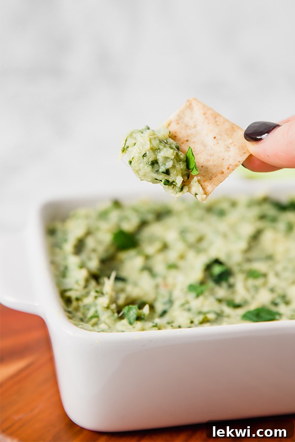 Person holding a chip dipped into a creamy paleo spinach and artichoke dip.