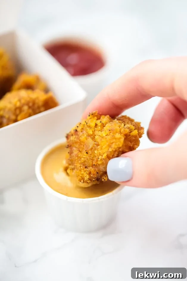Person dipping a golden-brown crispy paleo chicken nugget into sauce.
