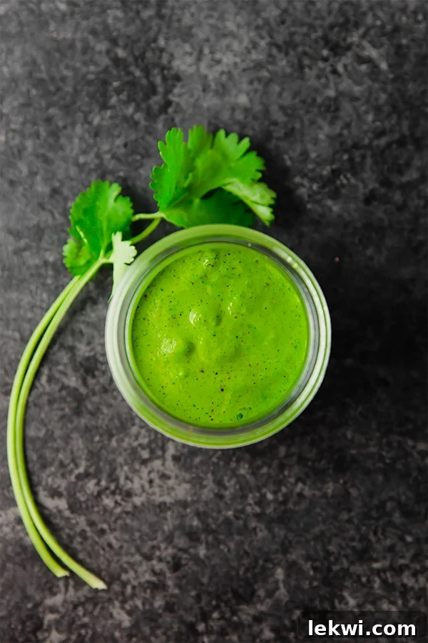 A glass jar filled with chimichurri sauce with fresh parsley next to it.