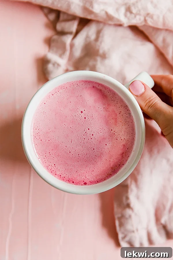 Person holding a mug of pink beet latte, showcasing its vibrant color.