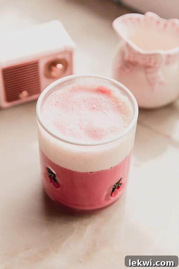 A small glass of vibrant pink beet latte, garnished with frothed milk.