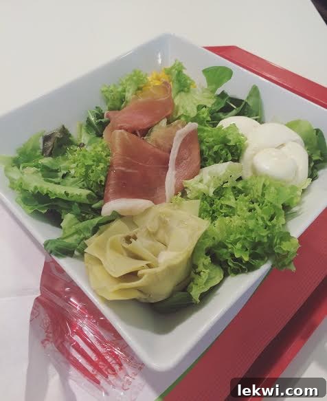 A salad with mozzarella, prosciutto, and artichokes in a bowl.
