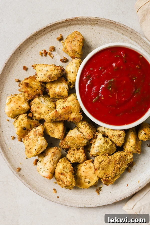 Crispy Italian chicken nuggets arranged around a bowl of marinara sauce, garnished with fresh herbs.