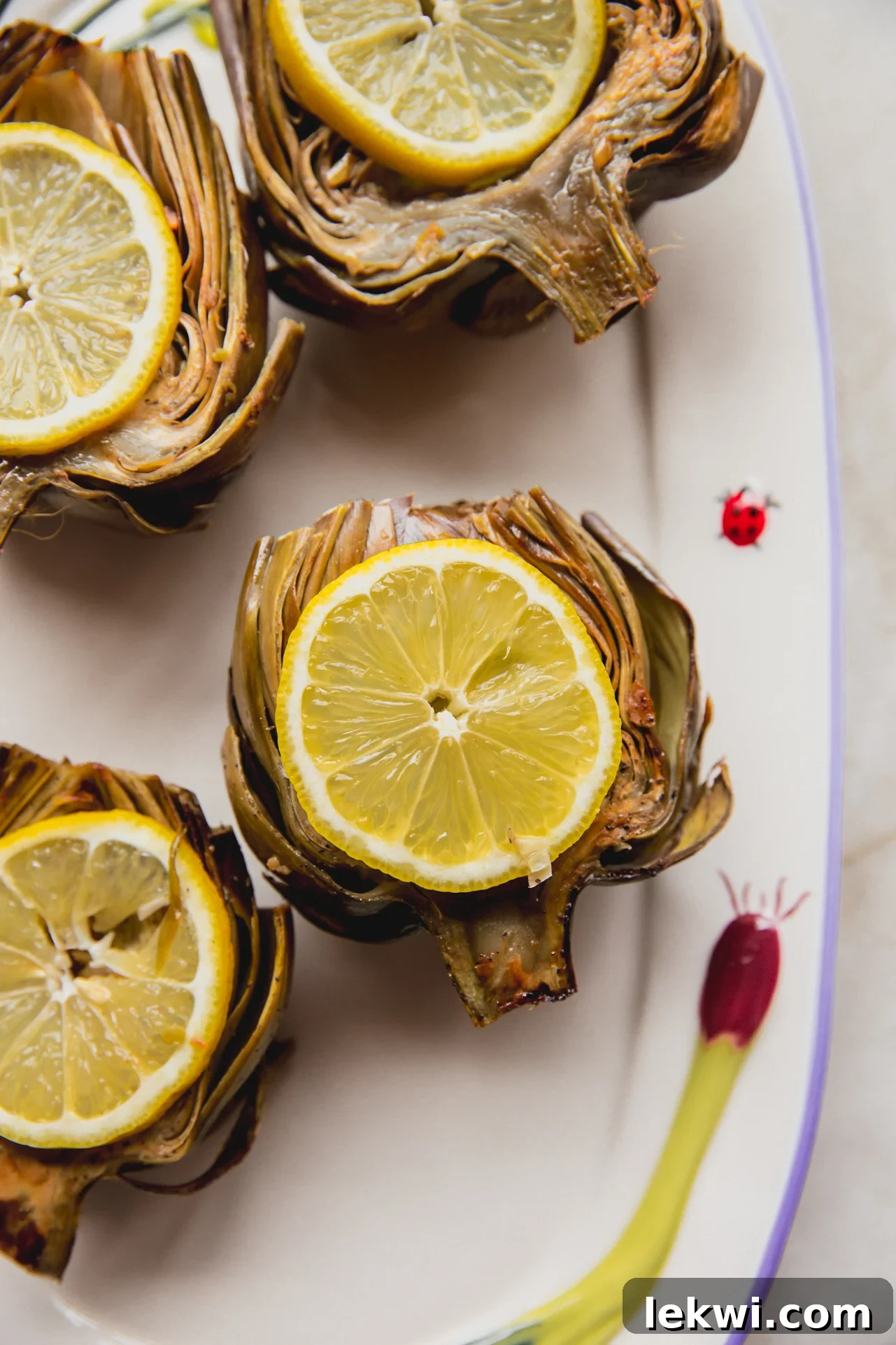 Four golden oven-baked artichokes beautifully arranged on a platter, garnished with fresh lemon slices.